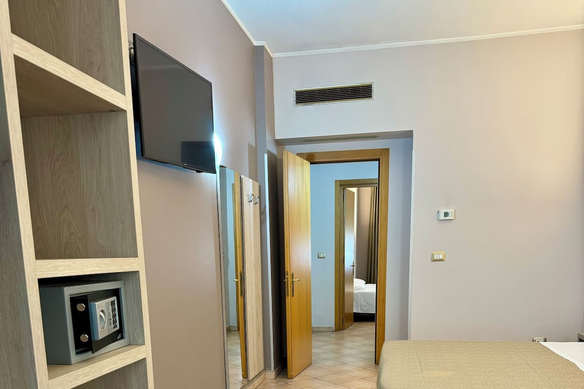 A hotel room with a bed, a TV mounted on the wall, a wardrobe, and a tiled floor.