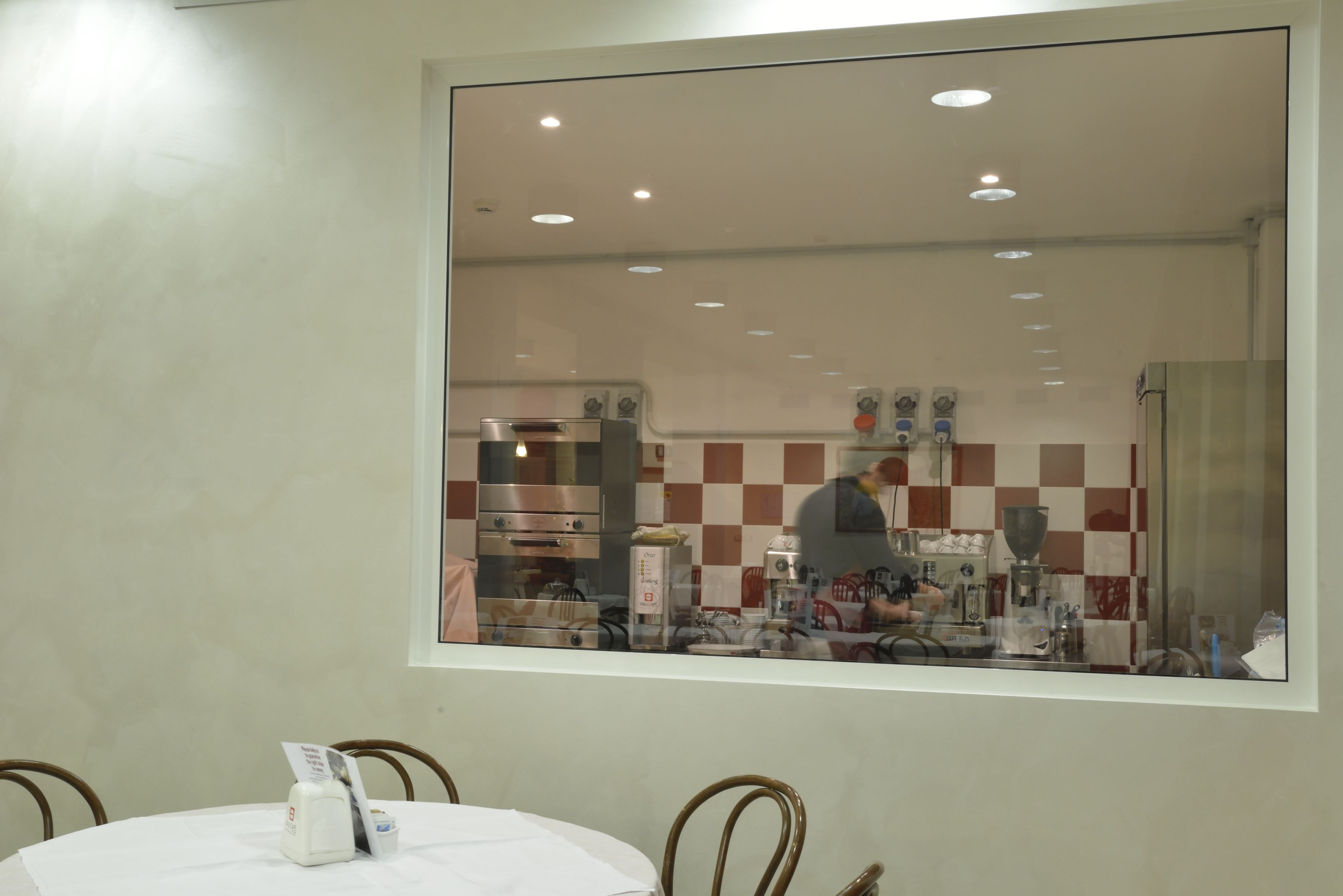 Un área de comedor con una mesa redonda, sillas y una ventana que da a una cocina con electrodomésticos y un salpicadero a cuadros.