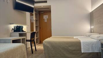 Ein Hotelzimmer mit zwei Betten, einem Schreibtisch mit Stuhl, einem an der Wand befestigten Fernseher und einer Holztür.