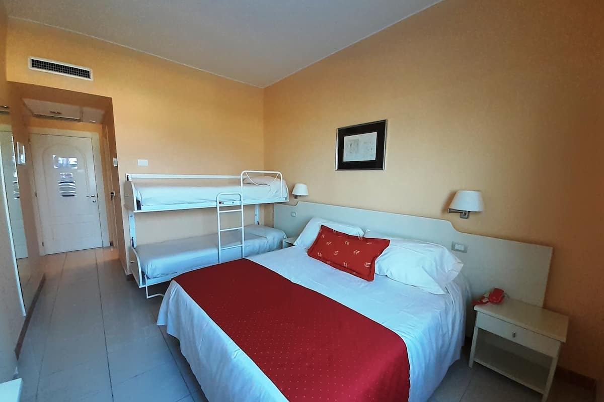 Habitación de hotel con una cama grande, una cama nido más pequeña, una mesita de noche y una puerta.