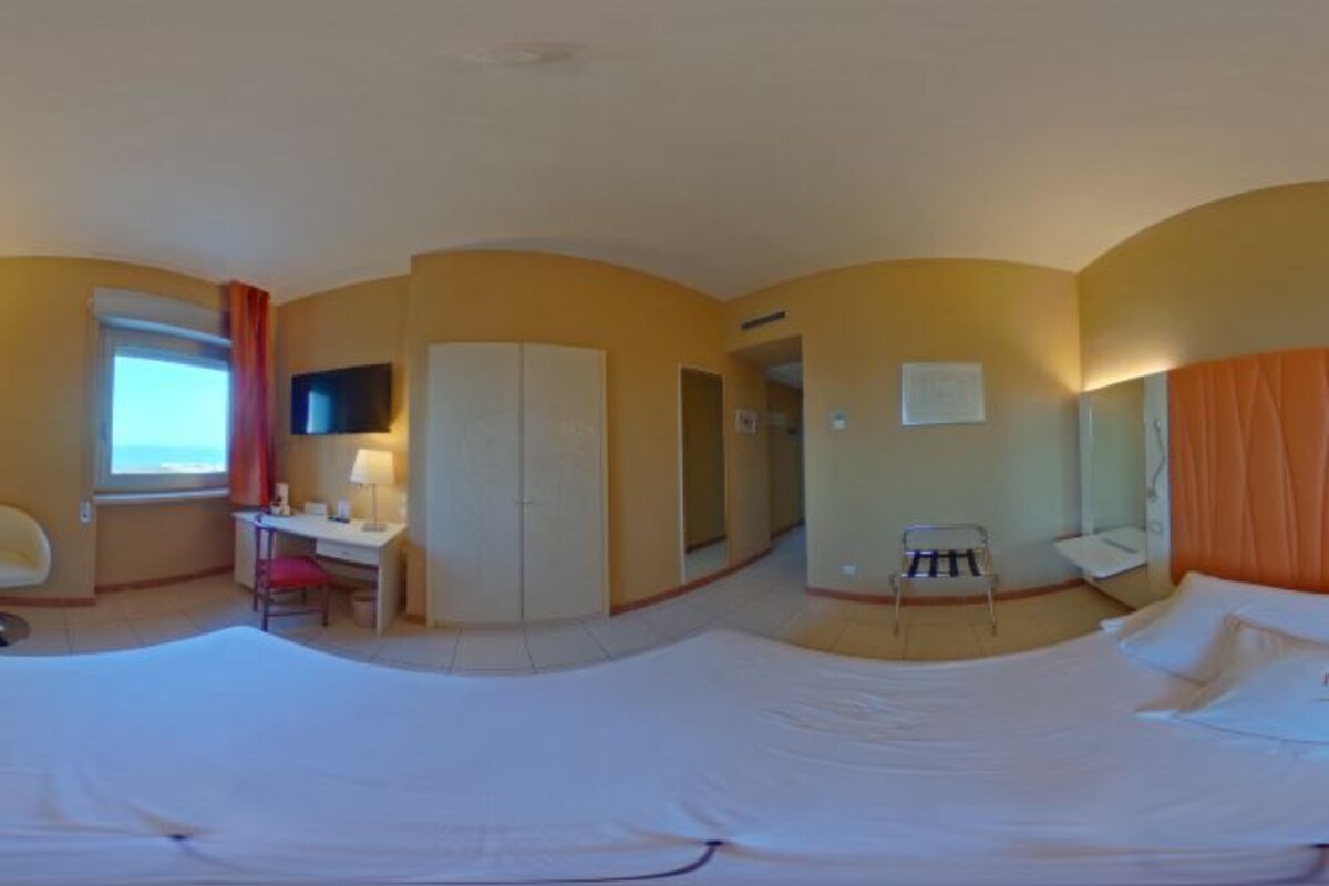 Ett hotellrum med en säng, ett skrivbord, en stol, en tv och ett fönster.