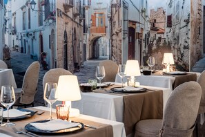 A restaurant with tables set for dining, featuring a view of a narrow street with buildings and an archway.