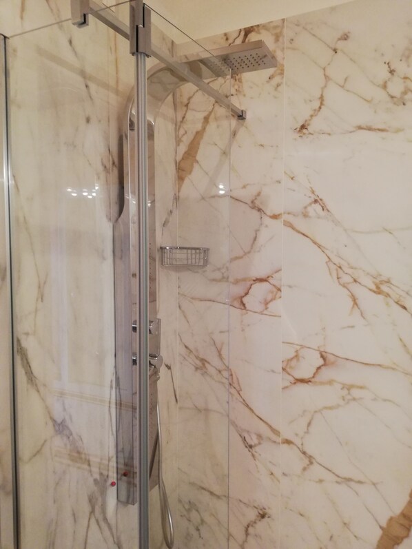 A glass-enclosed shower with a marble wall.