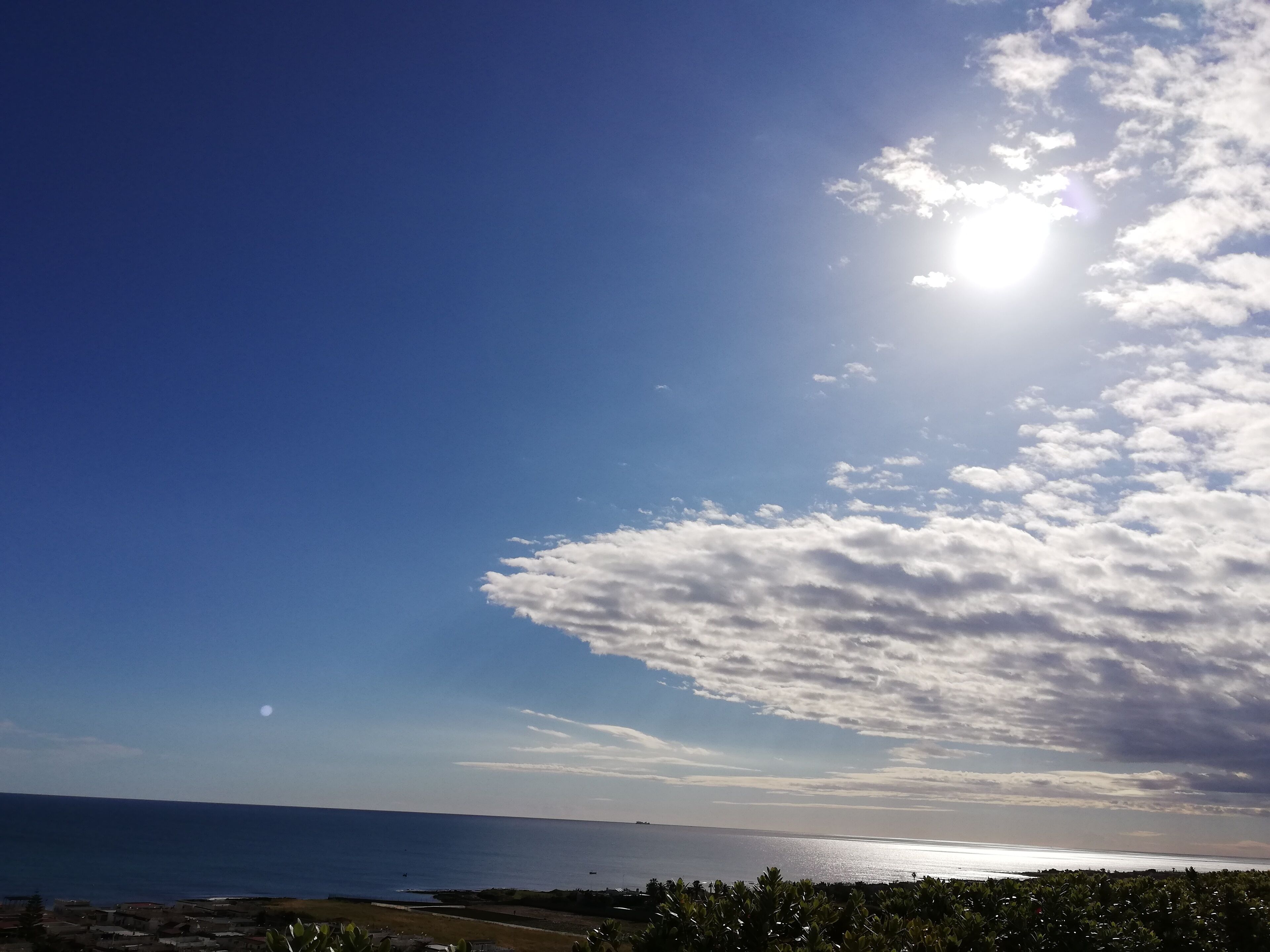 Eine Küstenlandschaft mit blauem Himmel, heller Sonne und Blick auf das Meer.