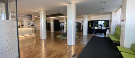 A spacious lobby with wooden flooring, white pillars, and green seating areas.