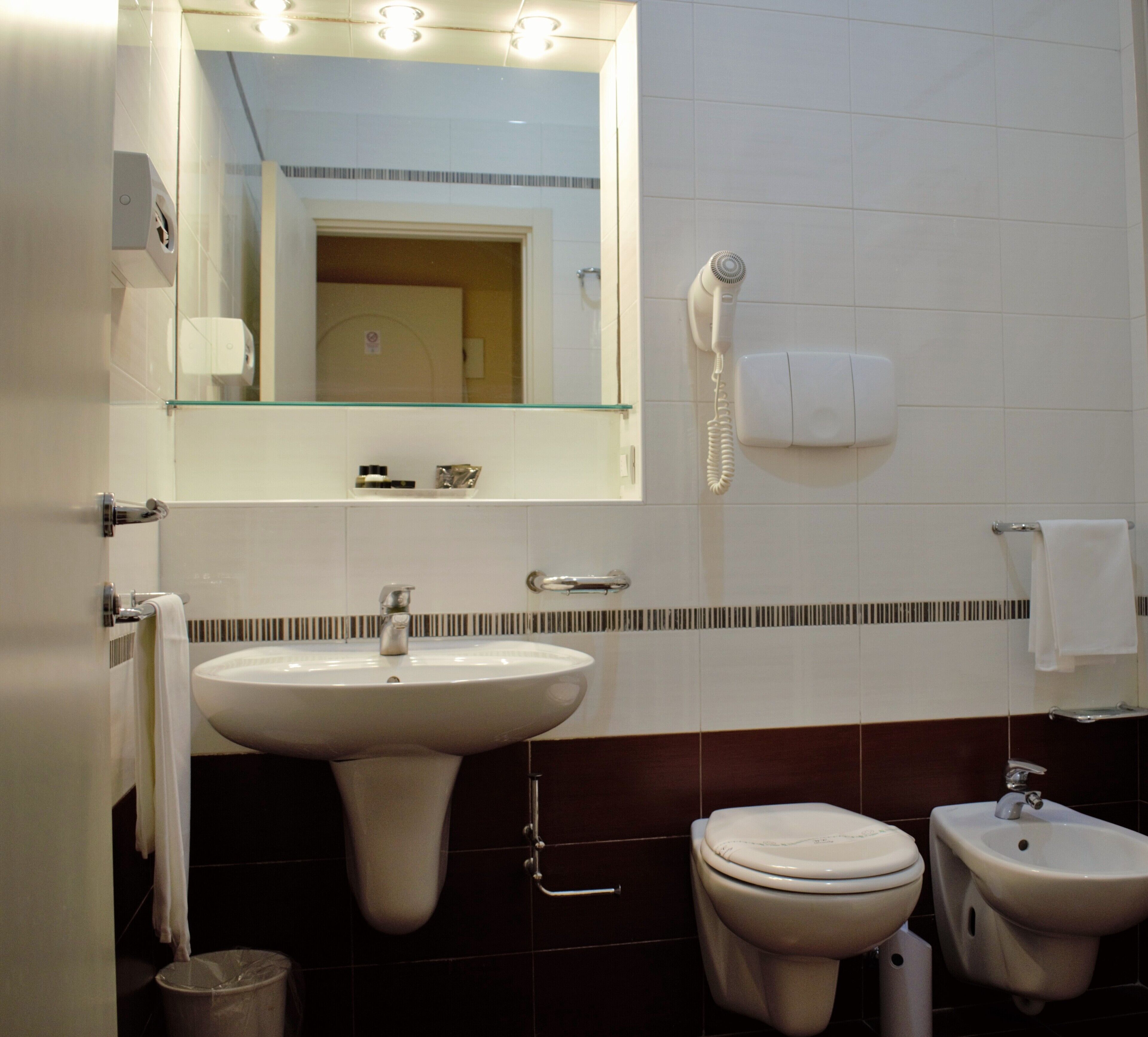 A bathroom with a sink, toilet, bidet, and a hairdryer mounted on the wall.