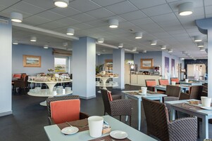 Un comedor amplio con varias mesas y sillas, con un diseño moderno, paredes azul claro y techos blancos.
