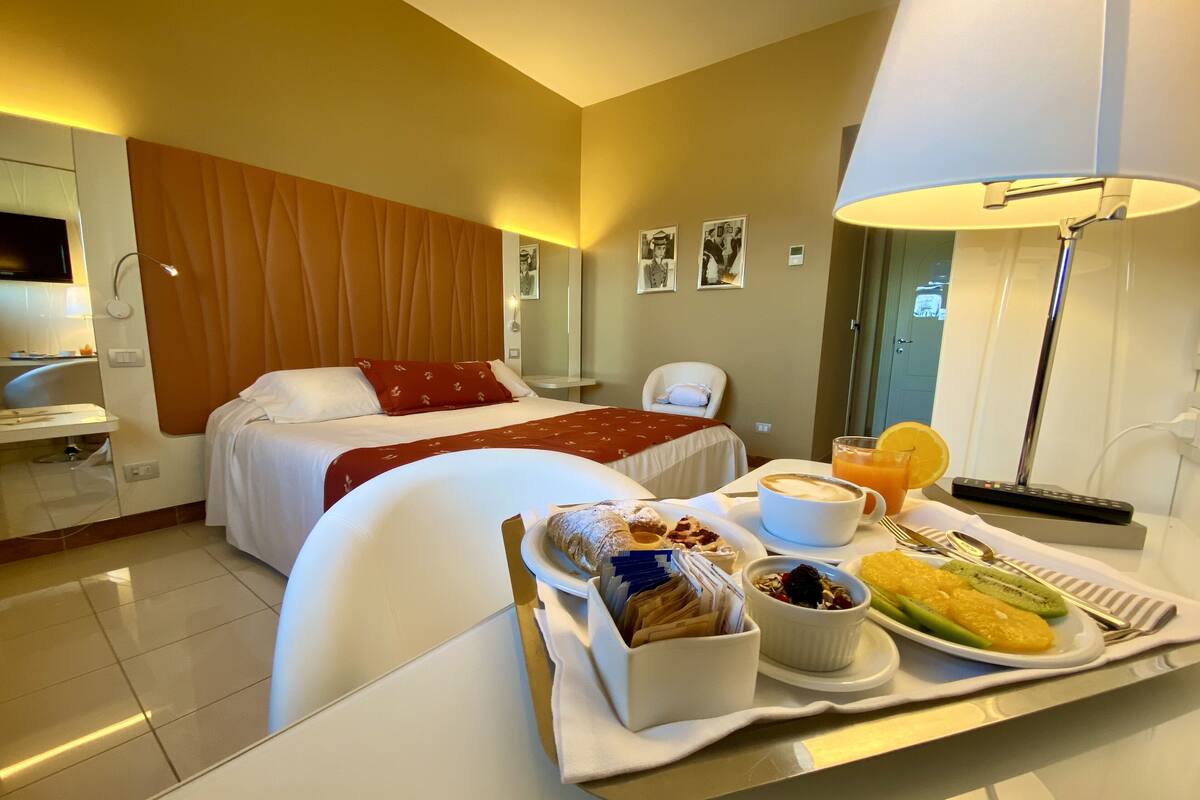 Habitación de hotel con cama, mesita de noche con bandeja de desayuno, una silla, un escritorio y una lámpara.