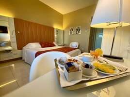 Habitación de hotel con cama, mesita de noche con bandeja de desayuno, una silla, un escritorio y una lámpara.