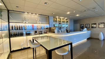 A modern bar area with a glass counter, bar stools, and a variety of bottles.