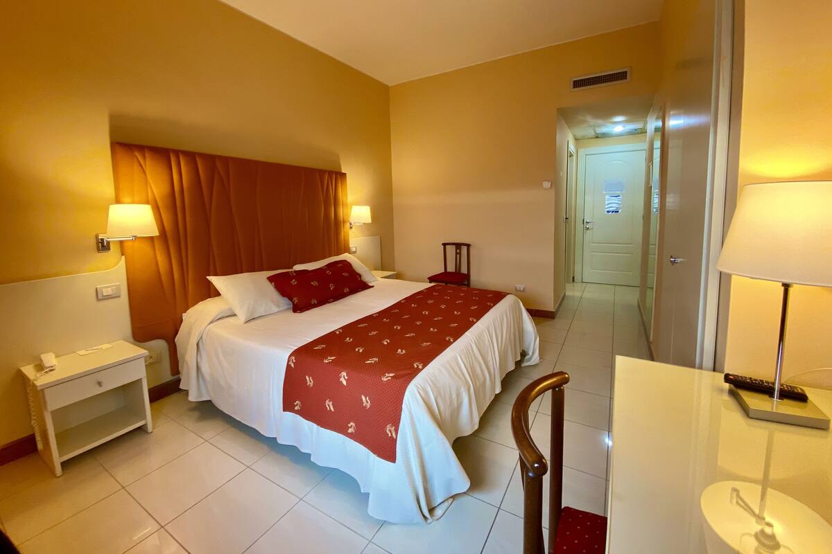 Una habitación de hotel con una cama, mesitas de noche, una silla y un escritorio con lámpara.