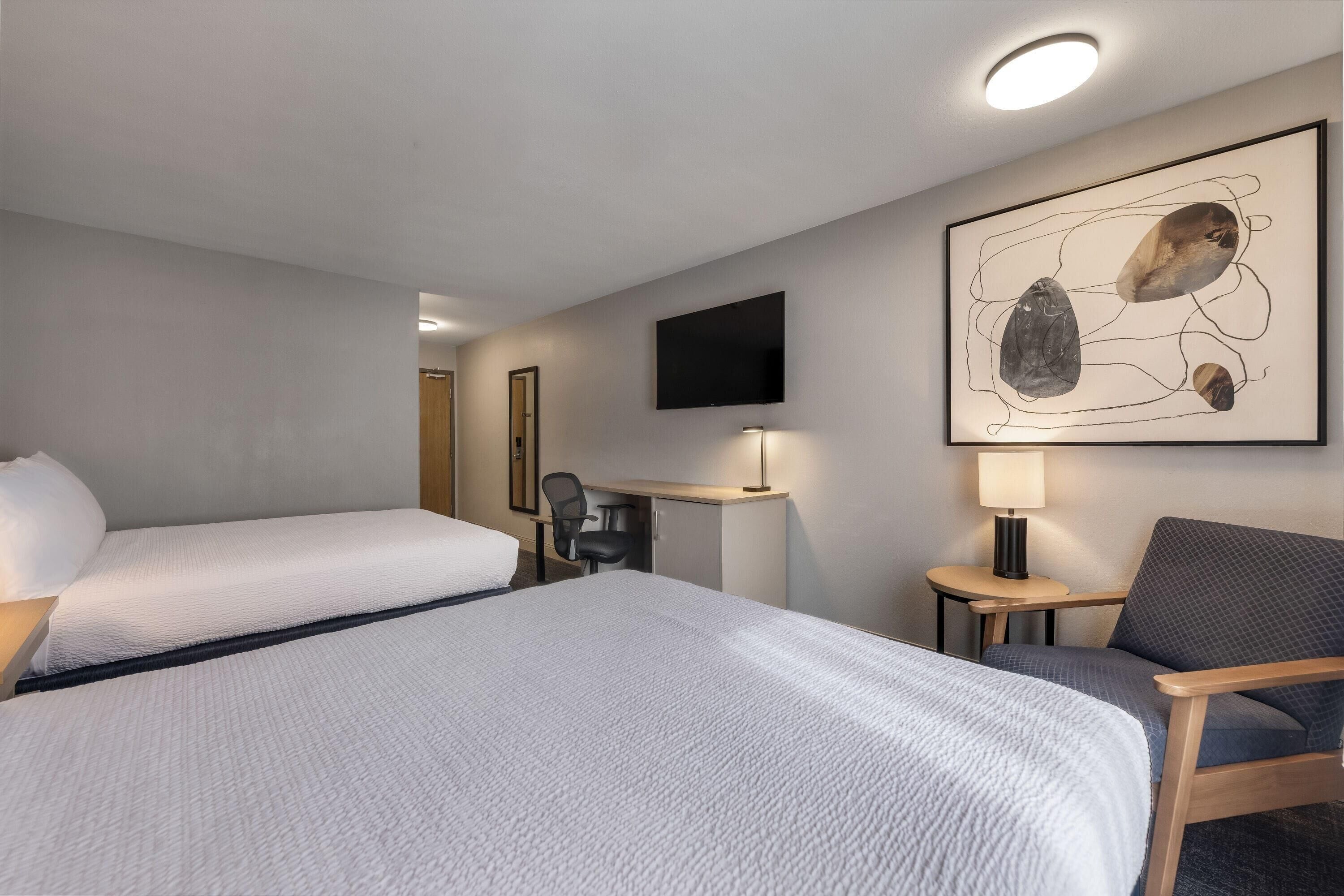 Une chambre d’hôtel avec deux lits, un bureau, une chaise, une télévision et une œuvre d’art murale.