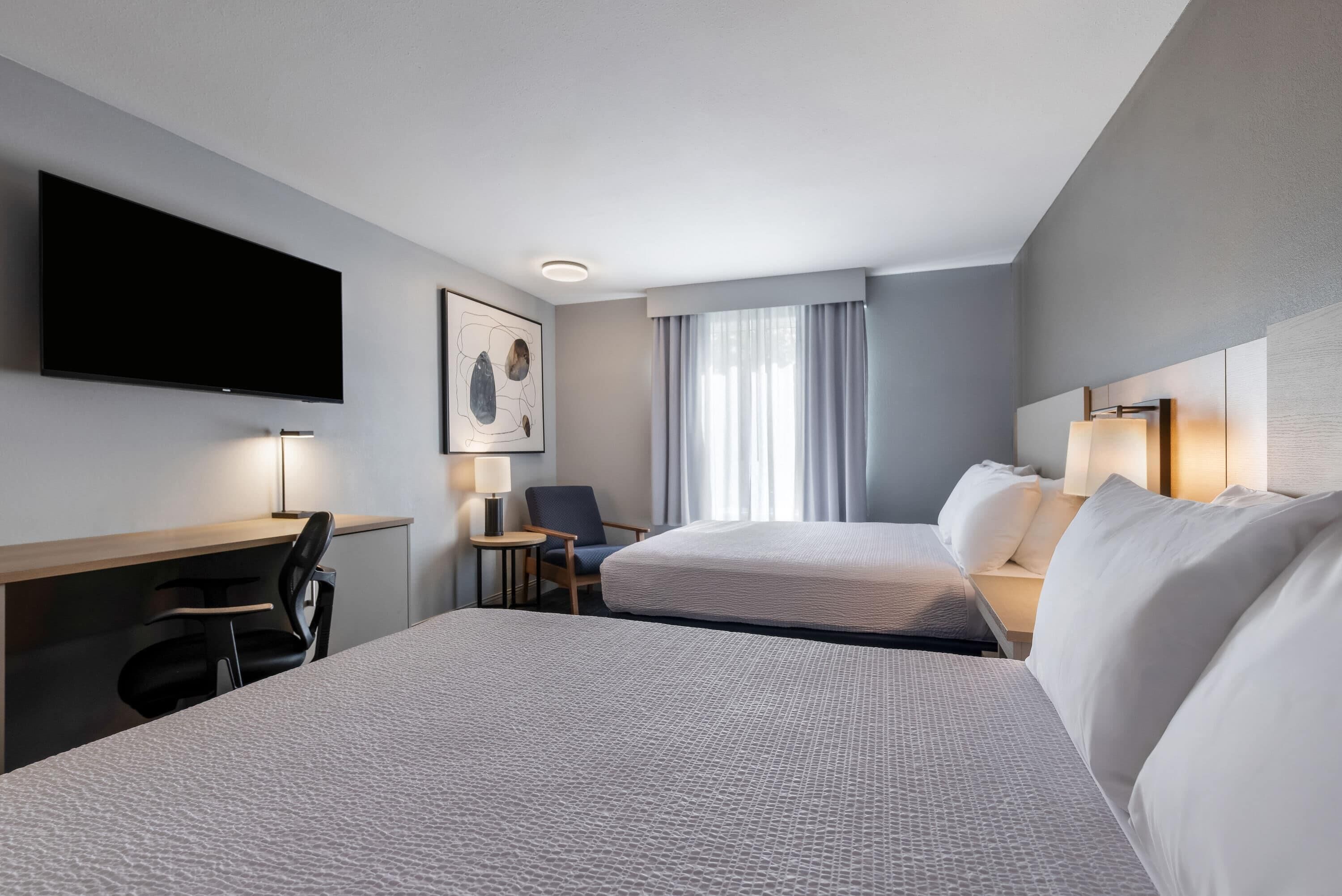 A hotel room with two beds, a desk, a chair, a TV, and a window with curtains.