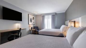 A hotel room with two beds, a desk, a chair, a TV, and a window with curtains.