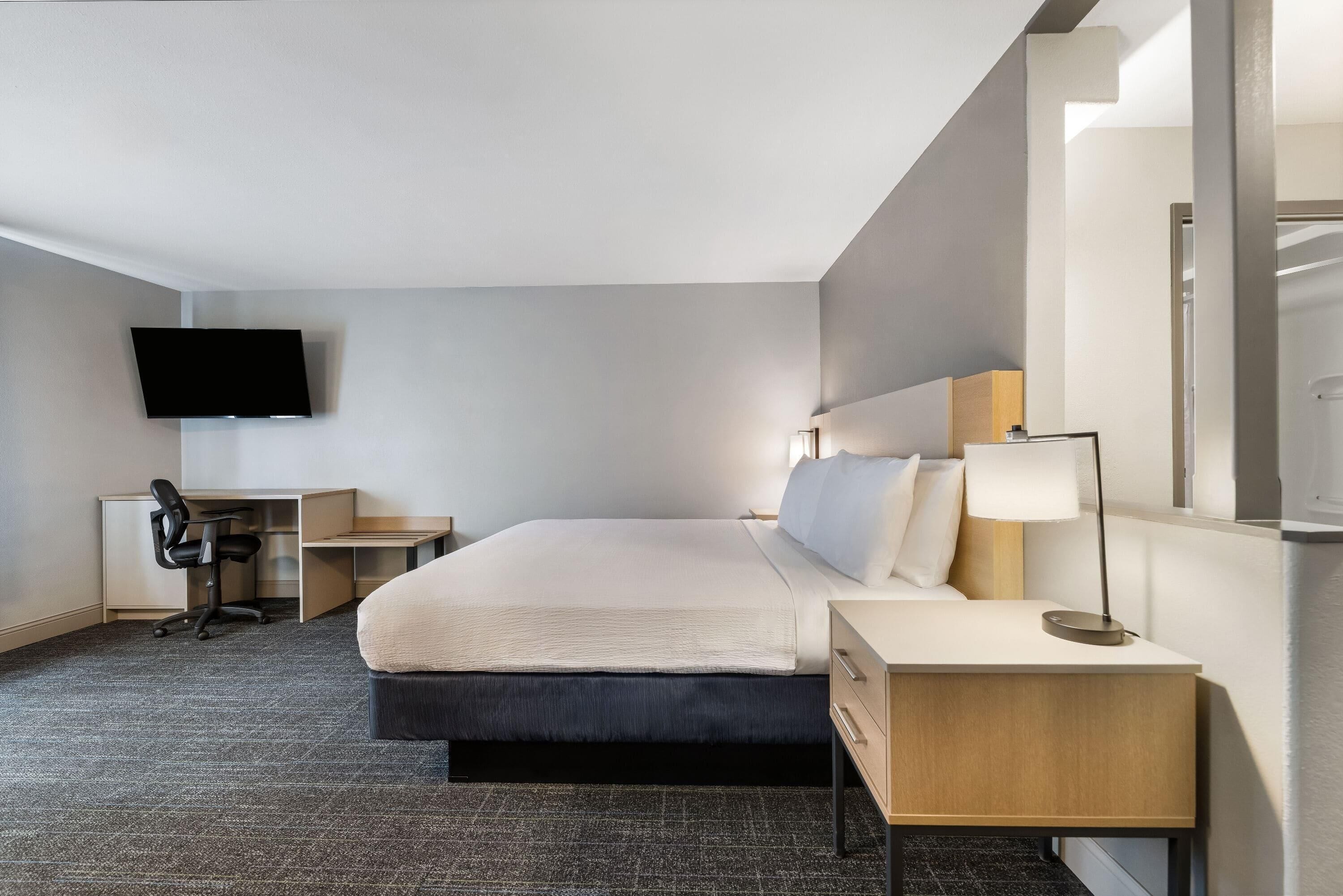 Habitació d'hotel amb un llit, escriptori, cadira, televisió, làmpada i mirall.