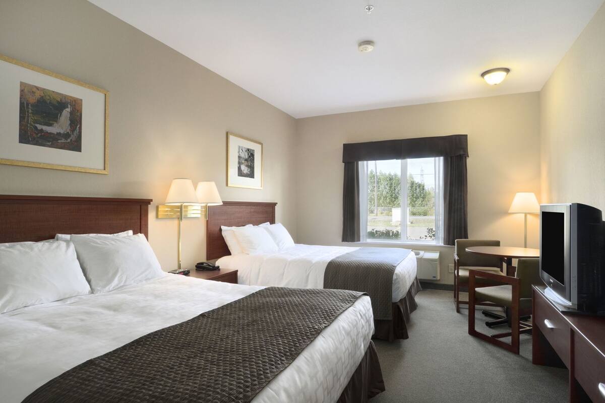 Une chambre d’hôtel avec deux lits, une télévision, un bureau et une fenêtre avec des rideaux.