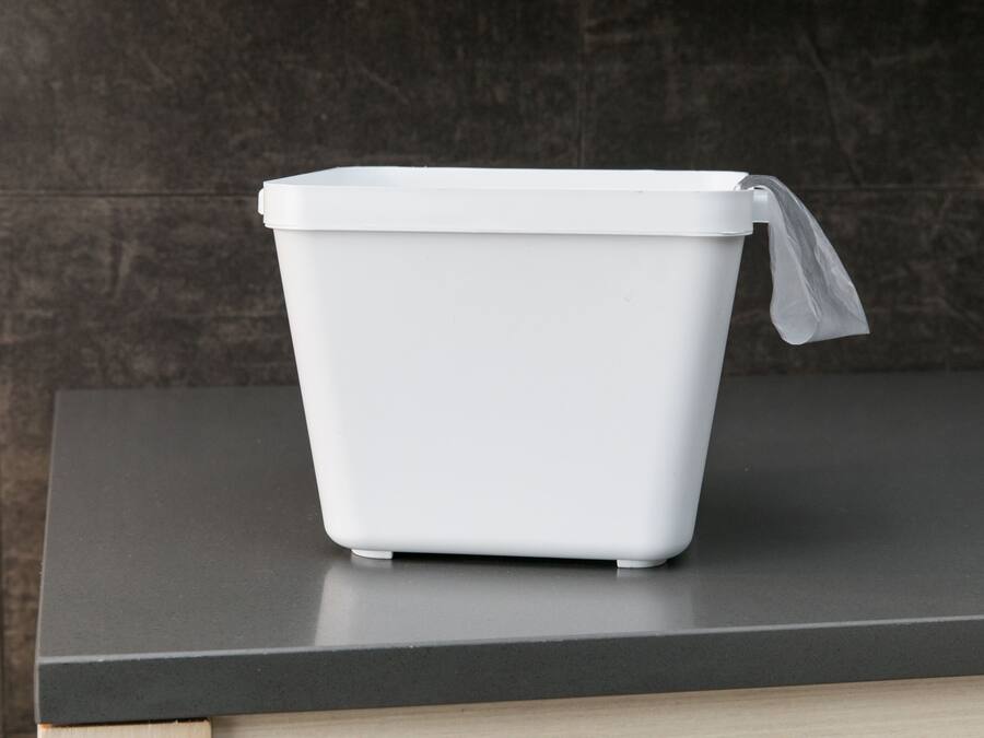 A white trash bin on a dark countertop.