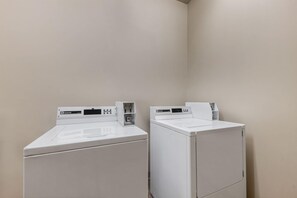 Two white front-loading washing machines in a corner with beige walls. - Days Inn by Wyndham Thunder Bay North (Thunder Bay)