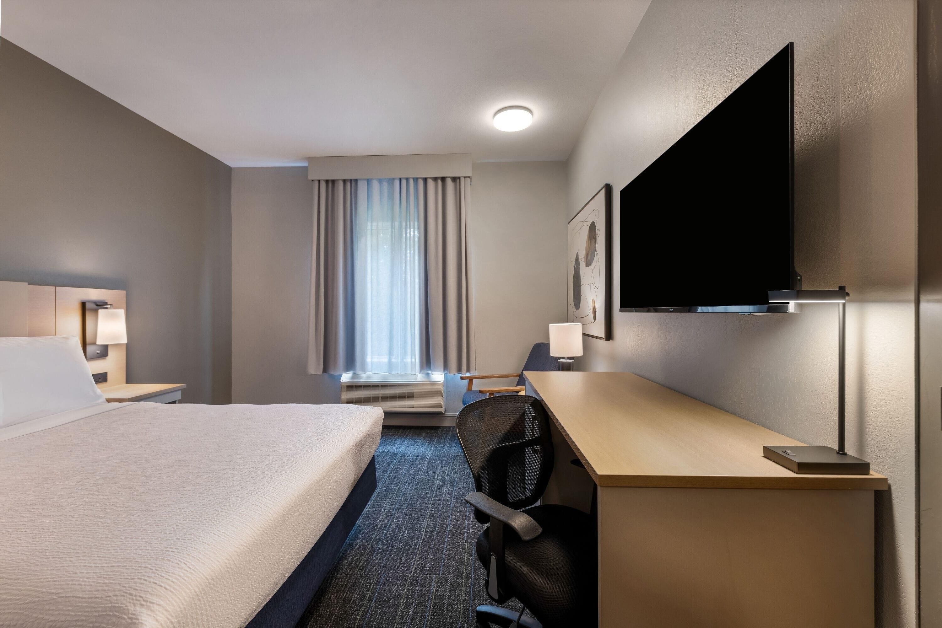 A hotel room with a bed, desk, chair, television, and a window with curtains.