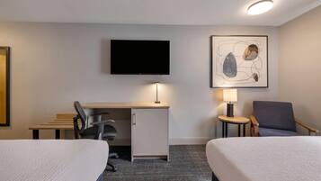 A hotel room with two beds, a desk, a chair, a television, and a lamp.
