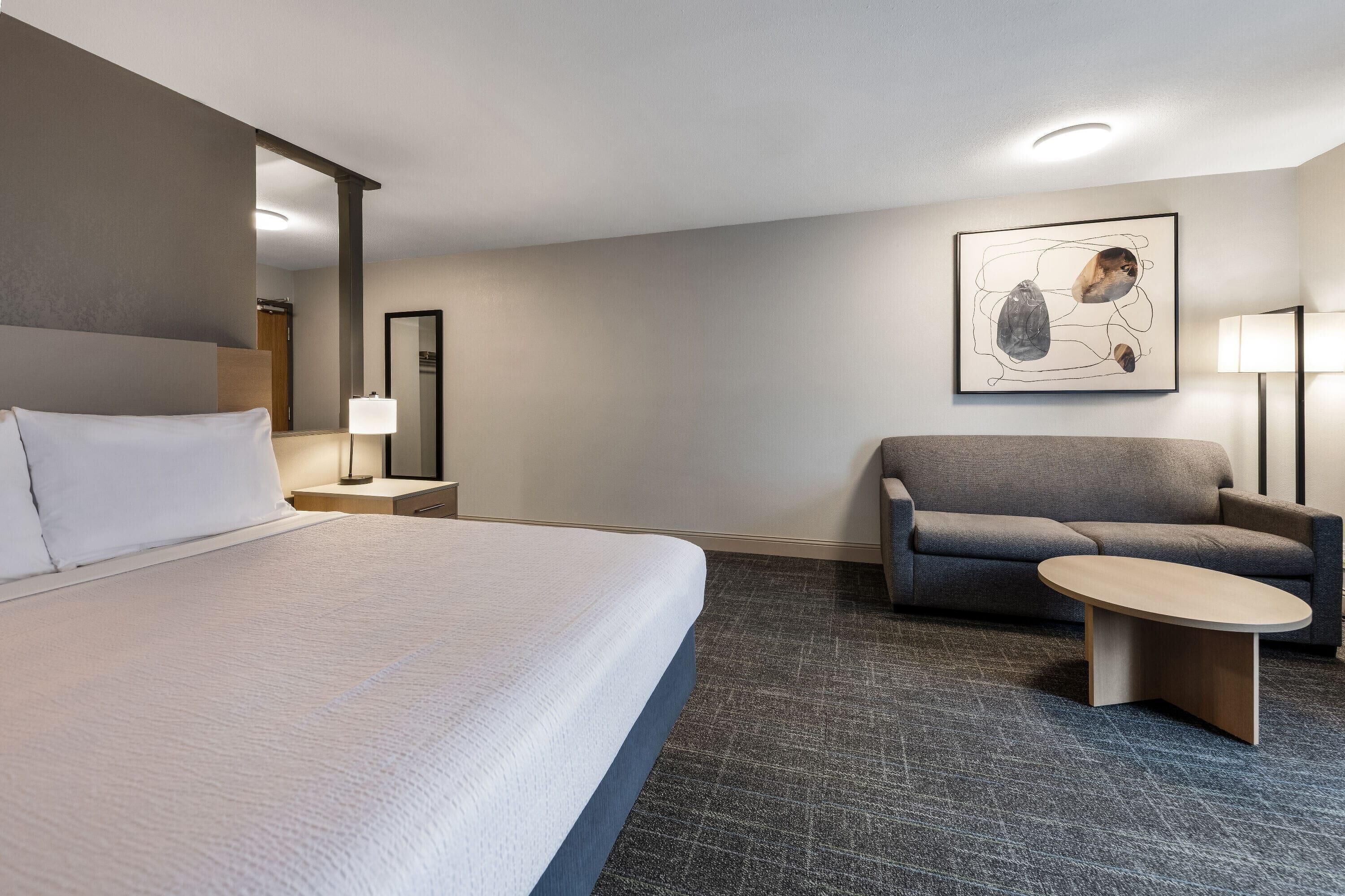 Une chambre d’hôtel avec un grand lit, un canapé, une petite table, une lampe et un tableau au mur.