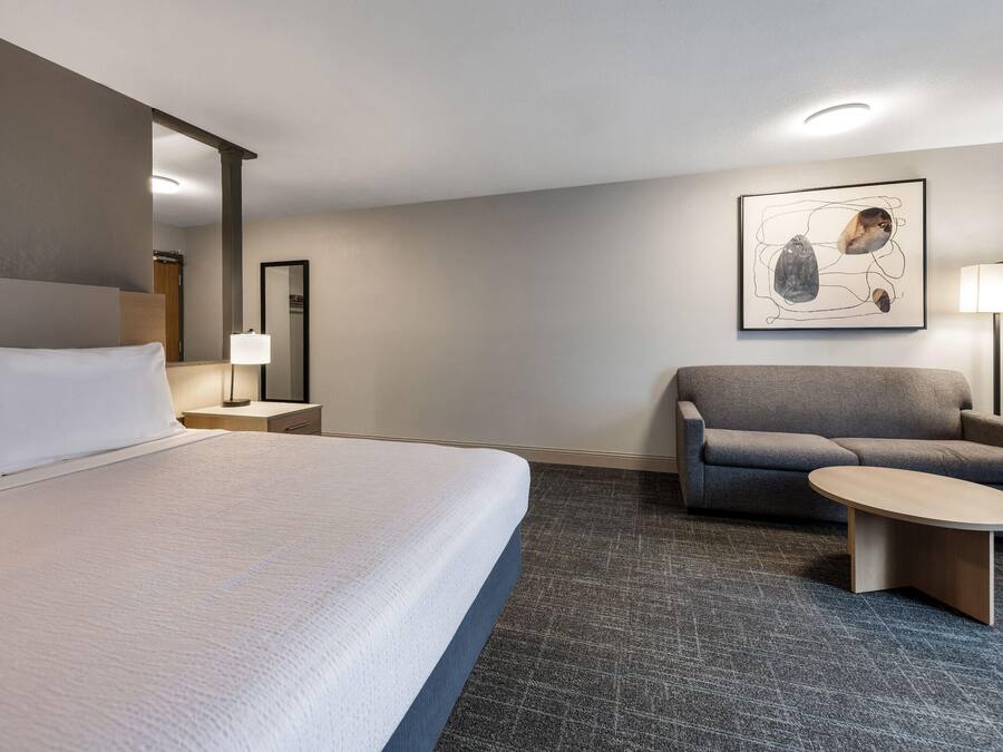 Une chambre d’hôtel avec un grand lit, un canapé, une petite table, une lampe et un tableau au mur.