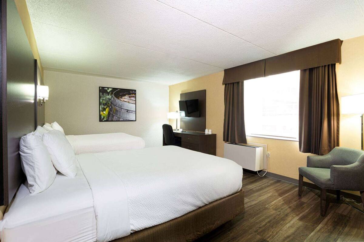 A hotel room with a large bed, a desk with a chair, a TV, and a window with curtains.