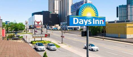 A Days Inn sign with a sun emblem, surrounded by city buildings and a parking lot with cars.