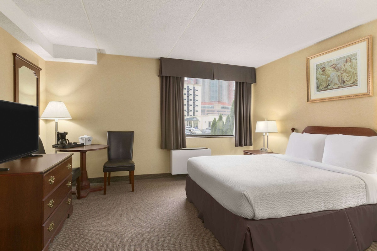A hotel room with a bed, a desk with a lamp, a chair, a television, and a window with curtains.