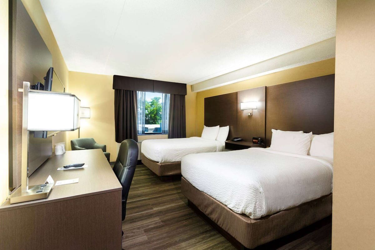 Une chambre d’hôtel avec deux lits, un bureau, une chaise, une télévision et une fenêtre avec des rideaux.