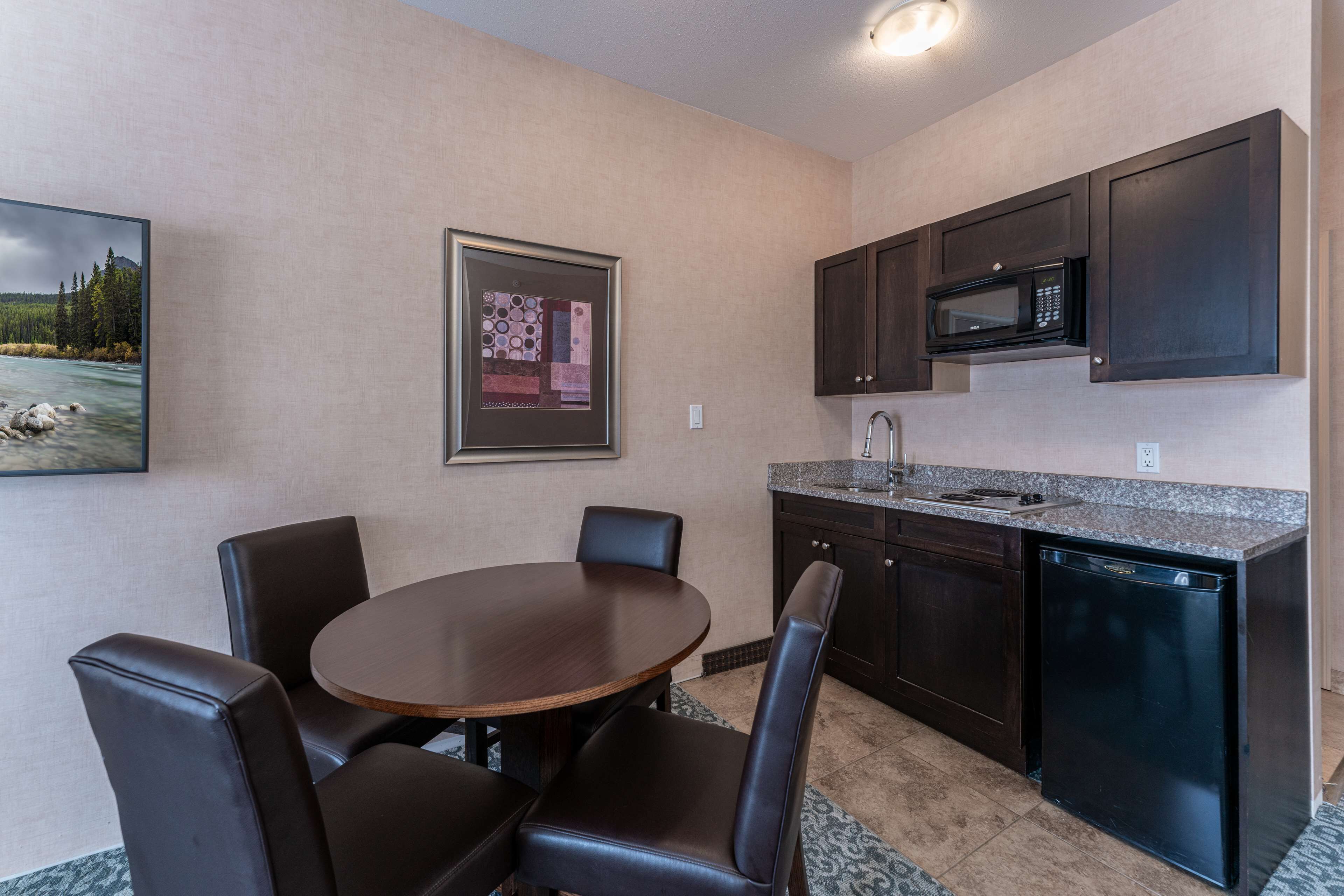 A modern kitchen with dark cabinets, a built-in microwave, and a granite countertop. There is a dining table with four chairs.