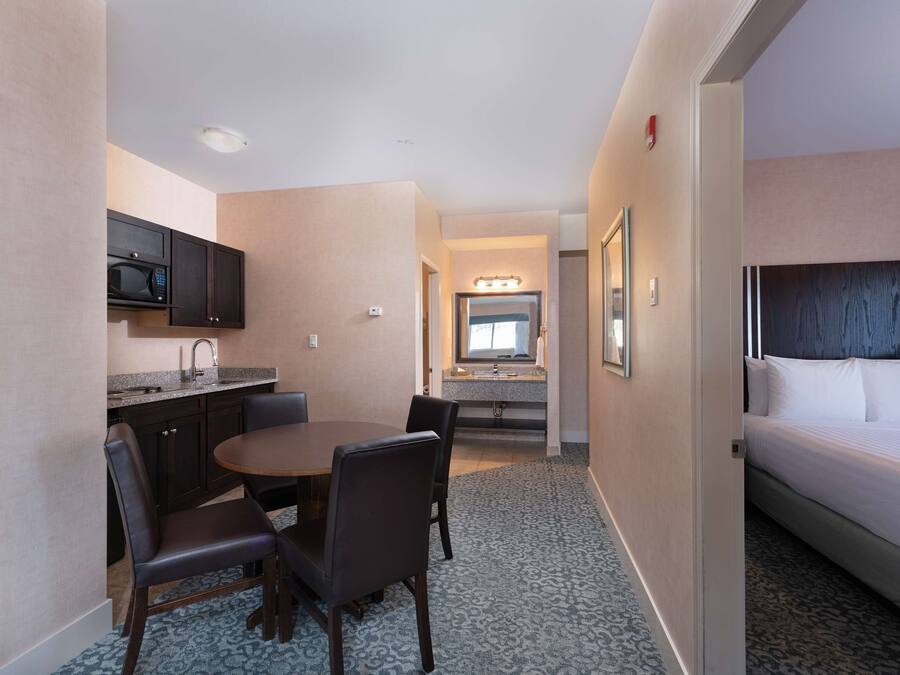 Hotelkamer met een bed, een badkamer met wastafel en spiegel, een kitchenette met magnetron en een eethoek met tafel en stoelen.