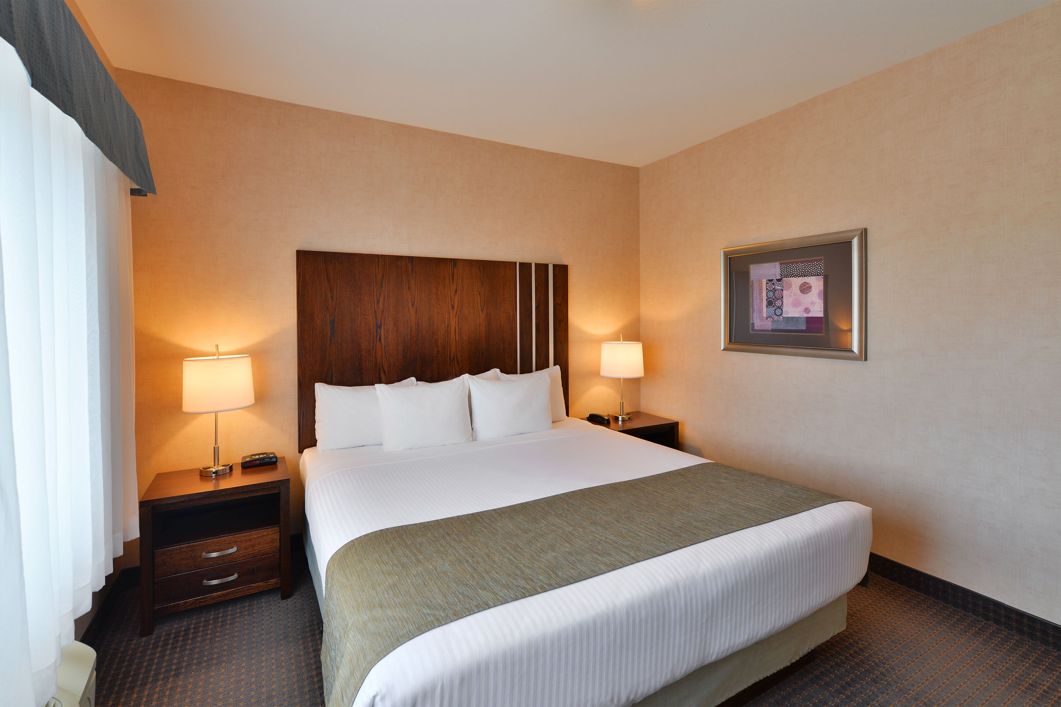 A hotel room with a large bed, two bedside tables with lamps, a framed picture on the wall, and a window with curtains.