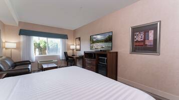 A hotel room with a large bed, a desk with a chair, a television, and a window with curtains.