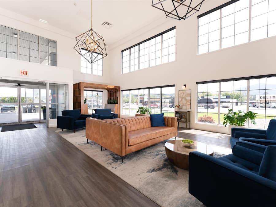 A spacious lobby with a leather sofa, blue armchairs, and a coffee table. Large windows offer views of the outside.