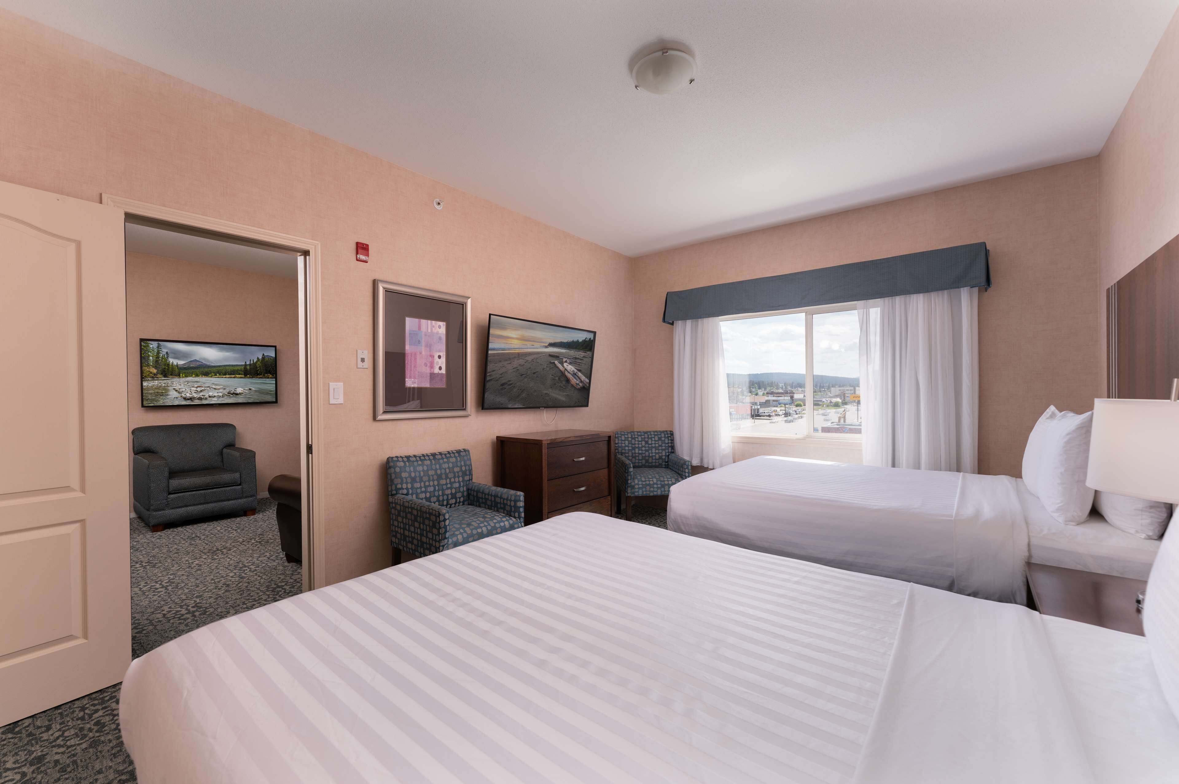 A hotel room with two beds, a desk, a chair, a television, and a window with a city view.