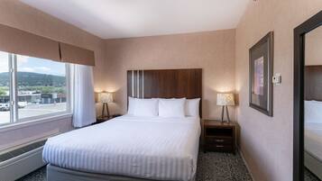 Habitación de hotel con una cama grande, dos mesitas de noche con lámparas, una ventana con cortinas e imagen enmarcadas en la pared.