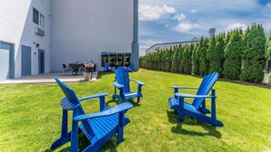A modern building with a flat roof, large windows, and a well-maintained lawn with blue Adirondack chairs.