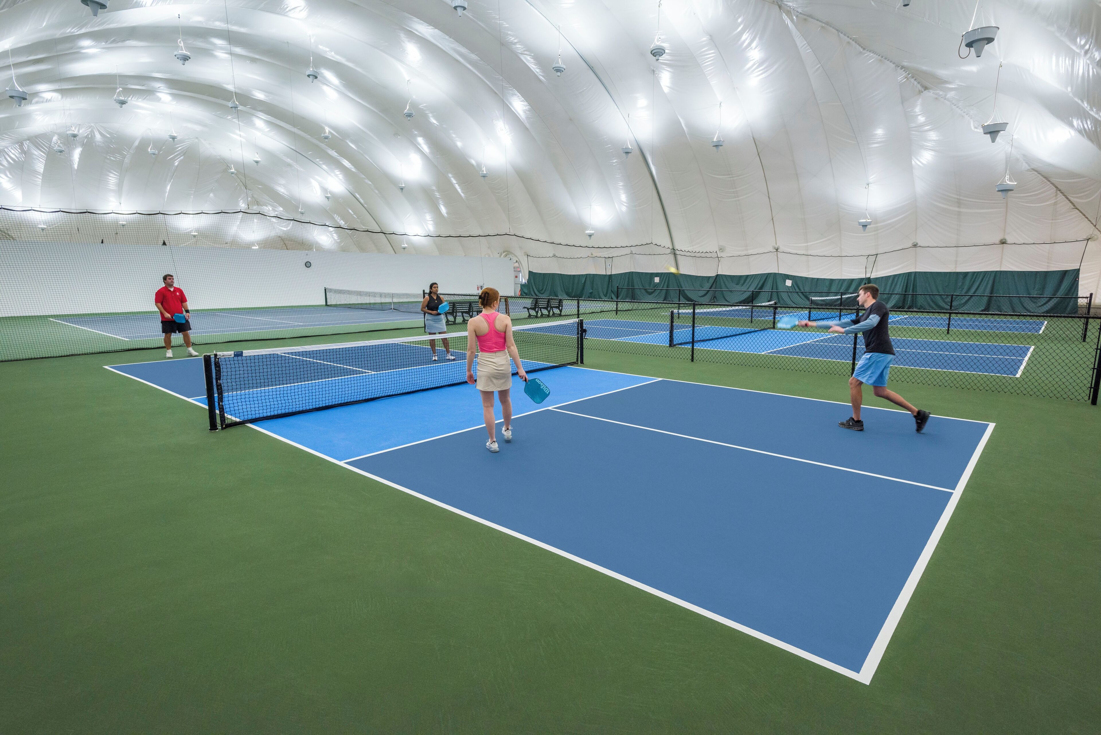 An indoor tennis facility with multiple courts, a net, and a dome ceiling.