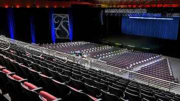 An auditorium with rows of seats, a stage with a blue curtain, and a large screen displaying a logo.