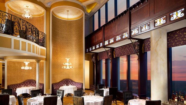 A luxurious dining area with round tables, elegant chairs, and a high ceiling with decorative lighting.