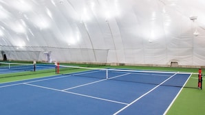 An indoor tennis court with multiple courts, a net, and a covered area with seating.