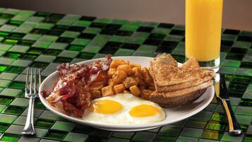 A breakfast plate with eggs, bacon, hash browns, toast, and a glass of orange juice on a checkered table.