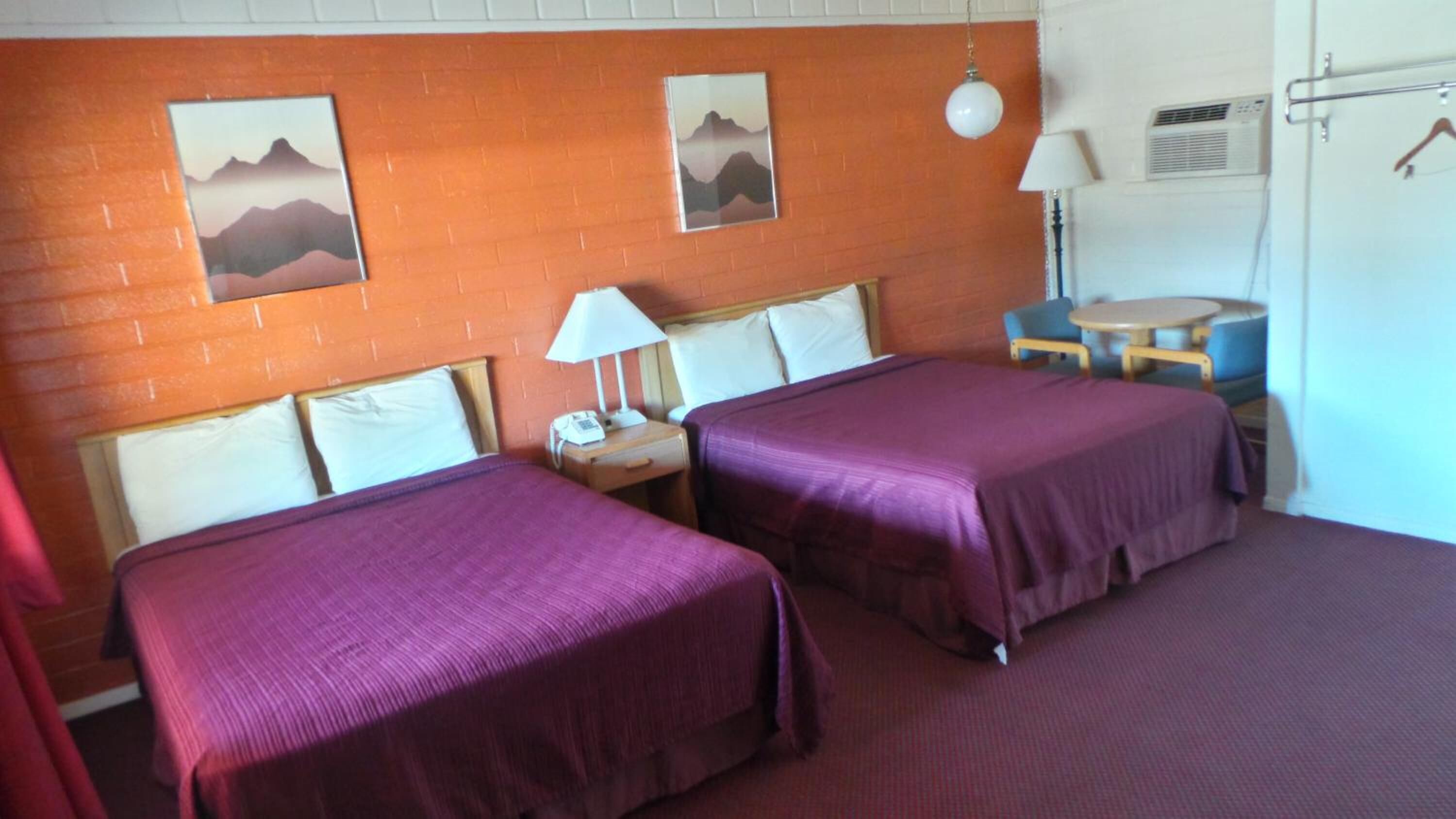 A hotel room with two beds, a small table, a chair, and a lamp.