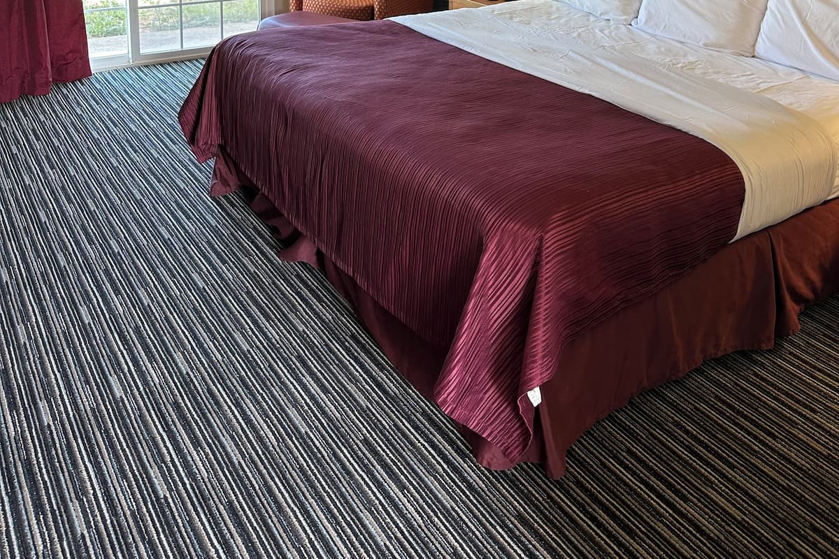 A hotel room with a large bed, a chair, a desk with a lamp, and a window with curtains.