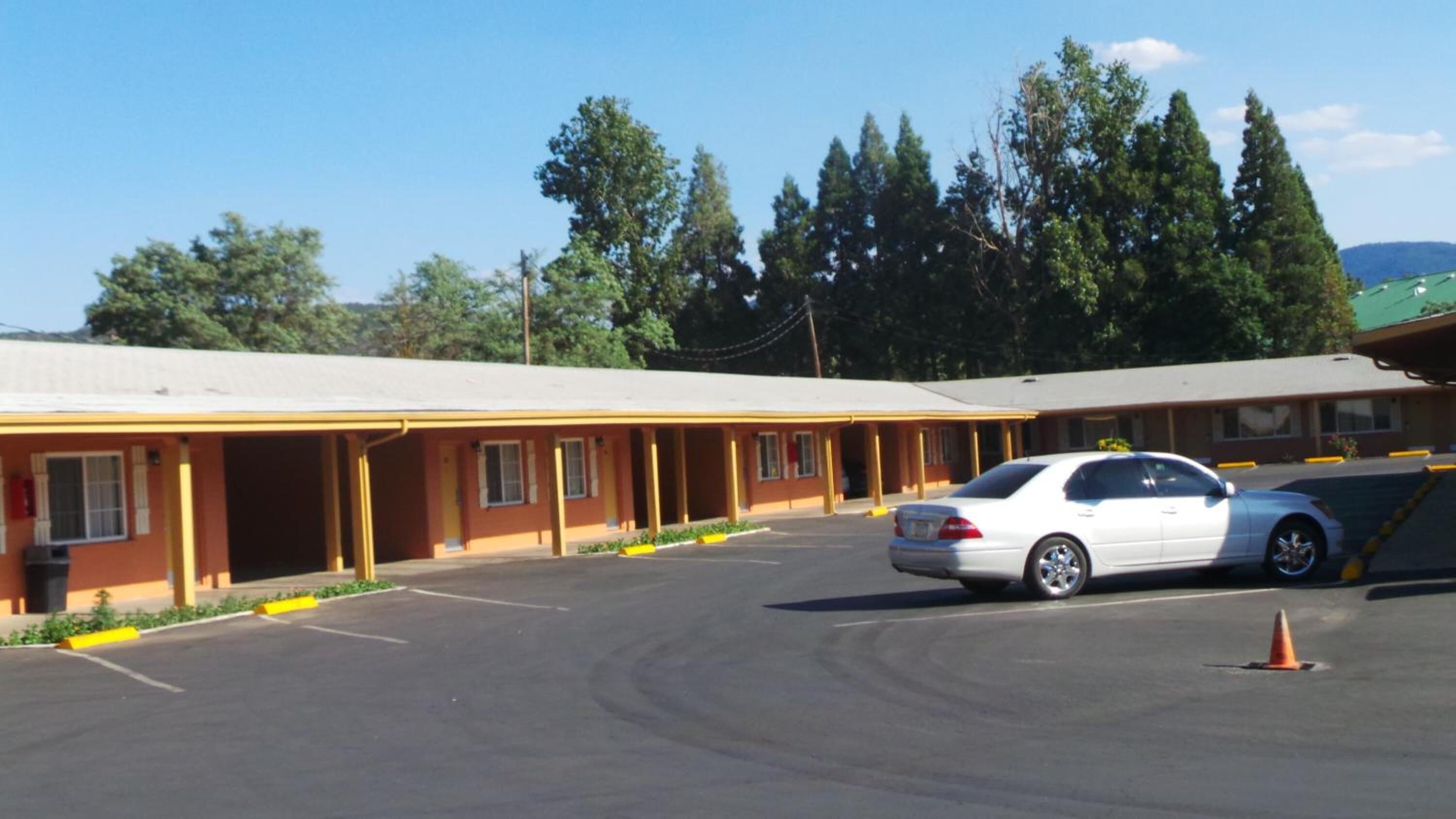 A motel with a single-story structure, a covered parking area, and a white car parked in the lot.