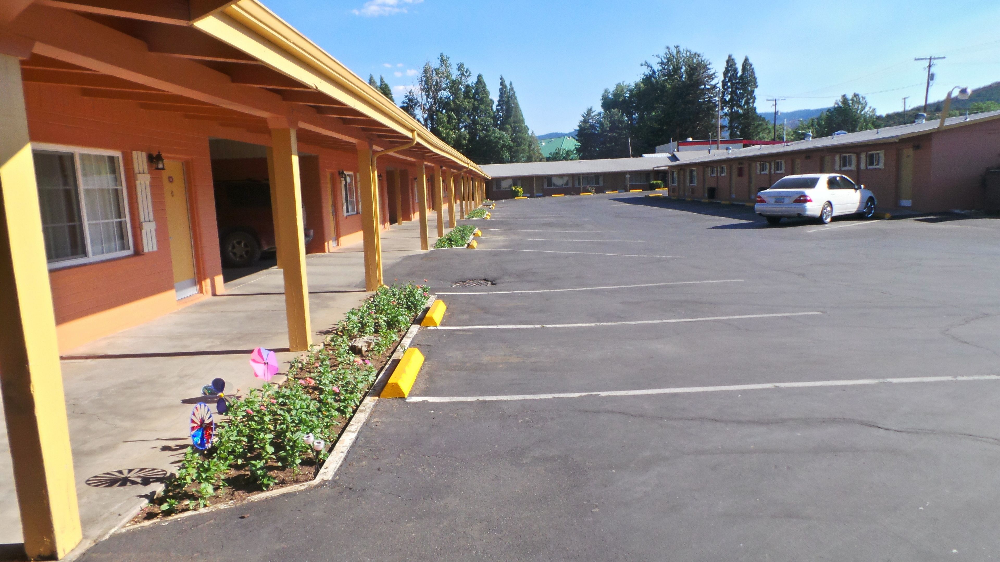 A motel with a row of rooms, a parking lot, and a white car parked in the lot.