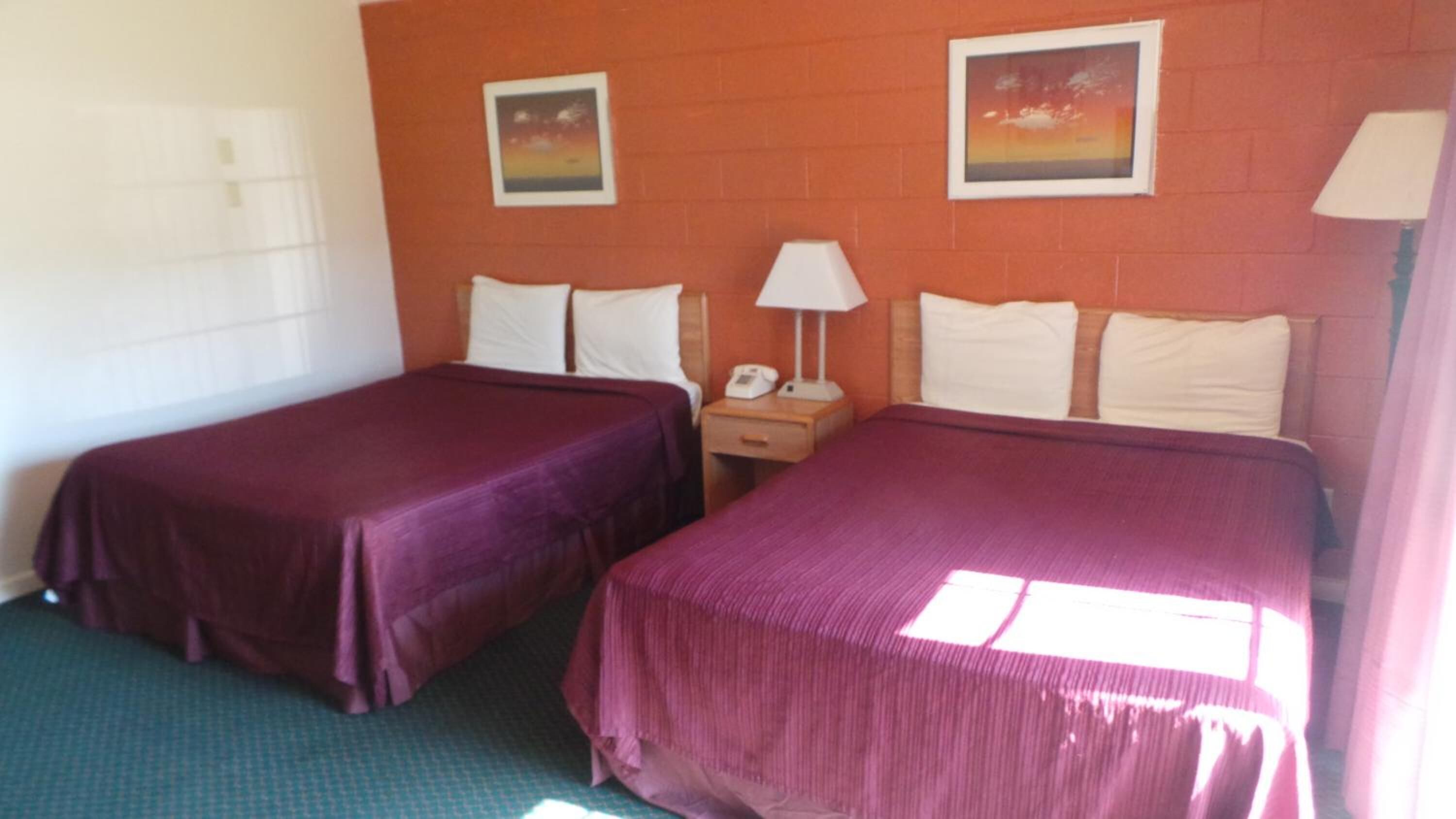 A hotel room with two beds, a nightstand with a lamp, and two framed pictures on the wall.