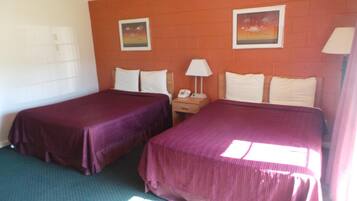 A hotel room with two beds, a nightstand with a lamp, and two framed pictures on the wall.