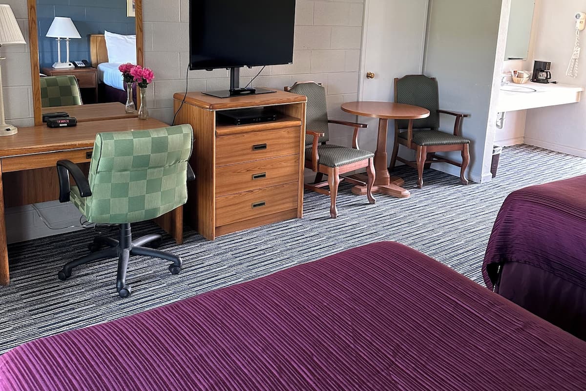 A hotel room with a bed, a desk with a chair, a television, a small table, and a mirror.